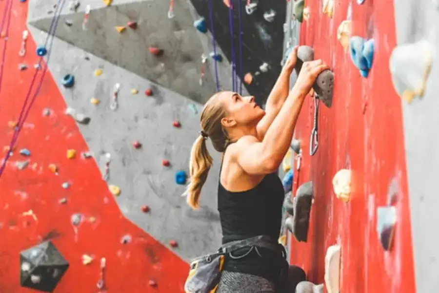 Sportswoman climber moving up on steep rock, climbing on artificial wall indoors. Extreme sports and bouldering concept
